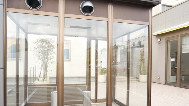 A modern building entrance with glass doors, metal bollards, and a clear view of the street outside. - Hotel Stay in Sanno Plaza (Tsuruoka)