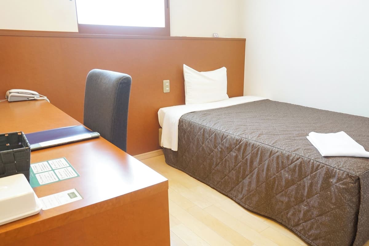 A hotel room with a bed, a desk with a phone, and a chair.