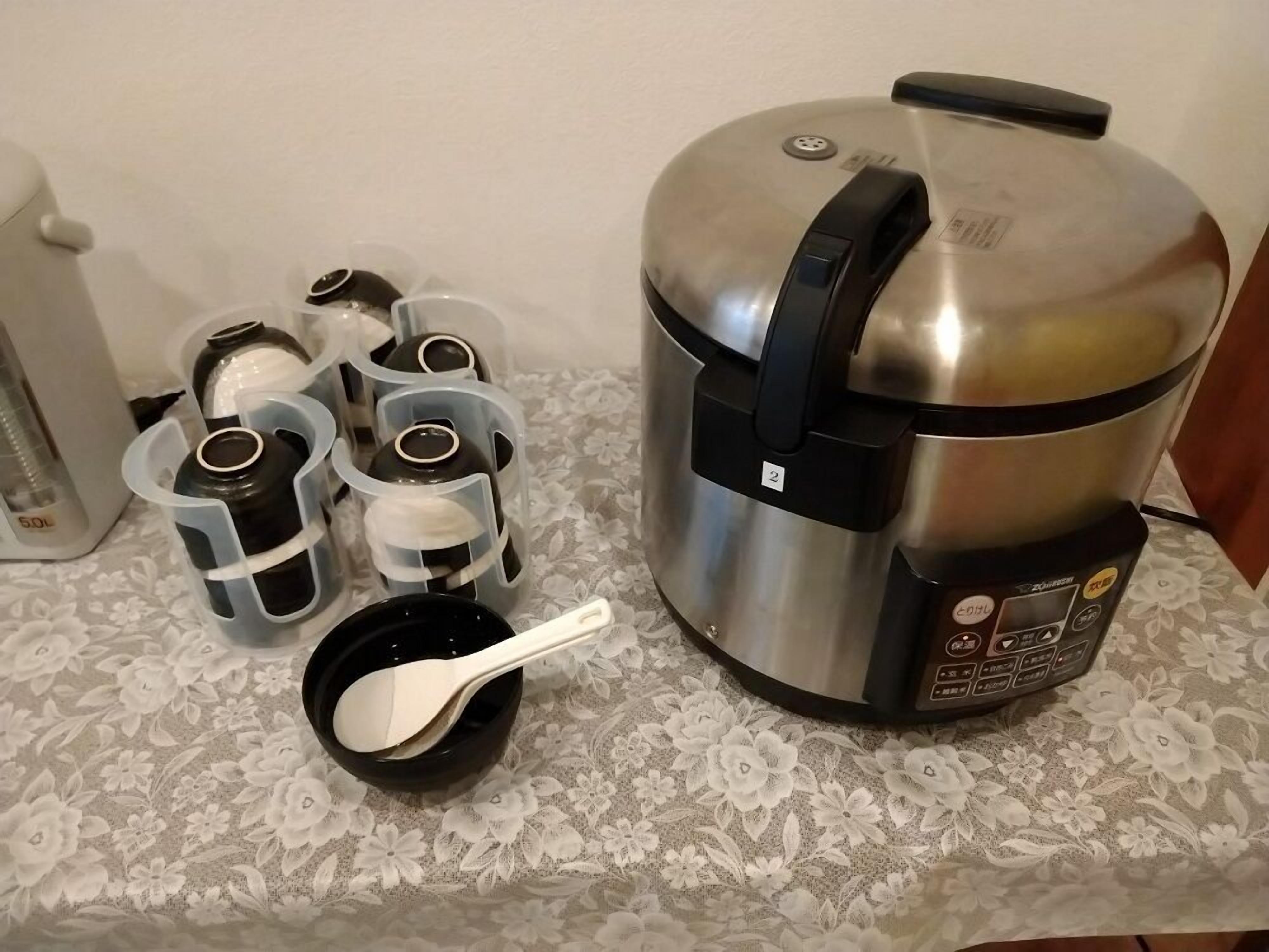 Une cuisine équipée d’un cuiseur à riz en acier inoxydable, d’un distributeur d’eau et d’une machine à café.