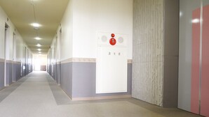A long, narrow hallway with doors on both sides, a fire alarm panel on the right wall, and a carpeted floor. - Hotel Stay in Sanno Plaza (Tsuruoka)