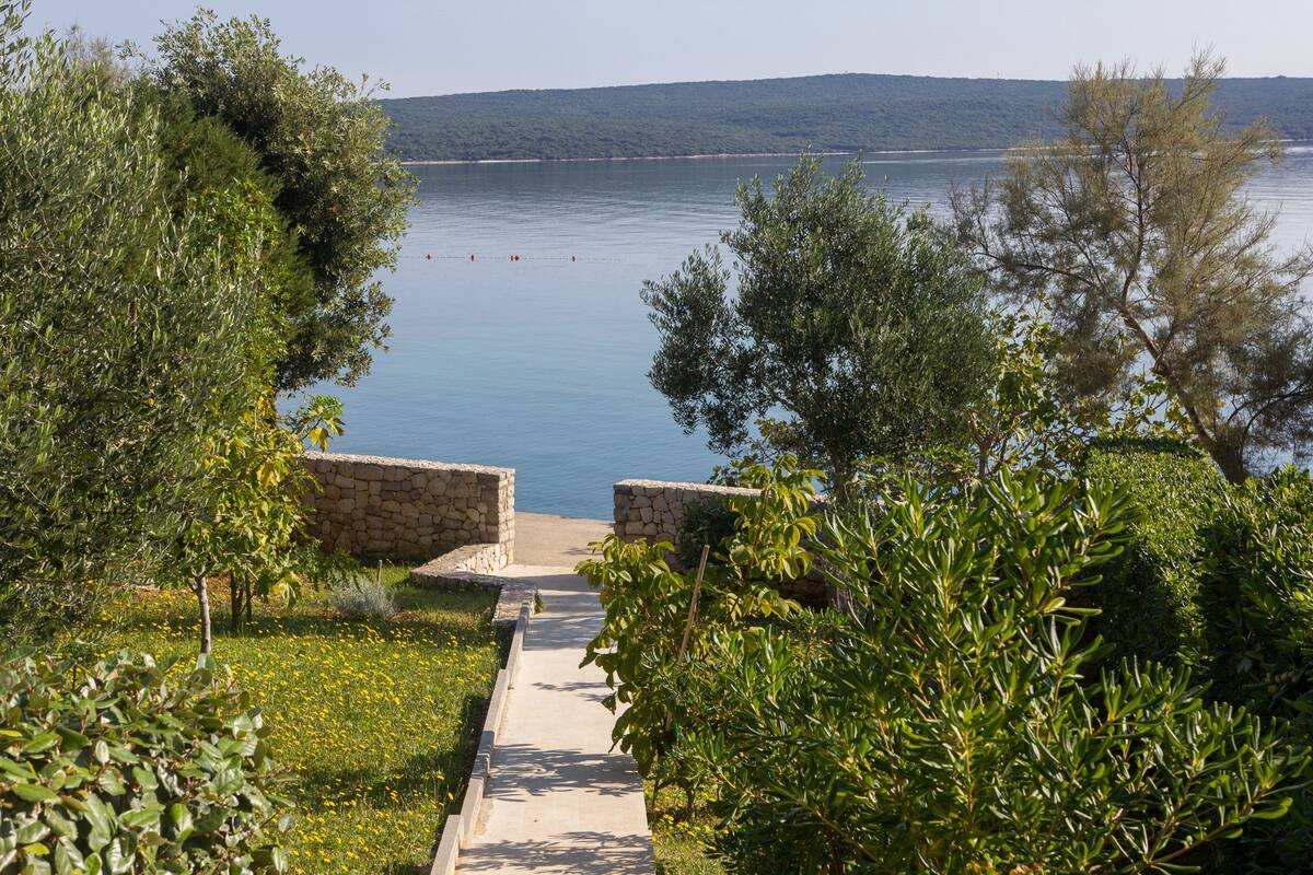 Un sentier qui mène à une plage bordée de murs de pierre et d’une végétation luxuriante.