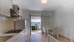 A modern kitchen with white cabinets, a built-in oven, and a dining area with a table and chairs. - Apartments Del Sole (Mali Losinj)