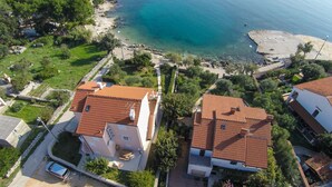 A coastal residential area with terracotta-roofed houses, clear blue sea, and green vegetation. - Apartments Del Sole (Mali Losinj)