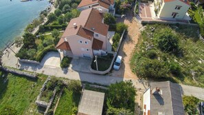 An aerial view of a residential area with a house featuring a tiled roof, a driveway, and a parked car.