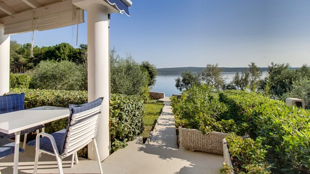 A patio with a table and chairs, a view of a lake, and a pathway surrounded by greenery. - Apartments Del Sole (Mali Losinj)