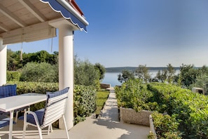 A patio with a table and chairs, a view of a lake, and a pathway surrounded by greenery.