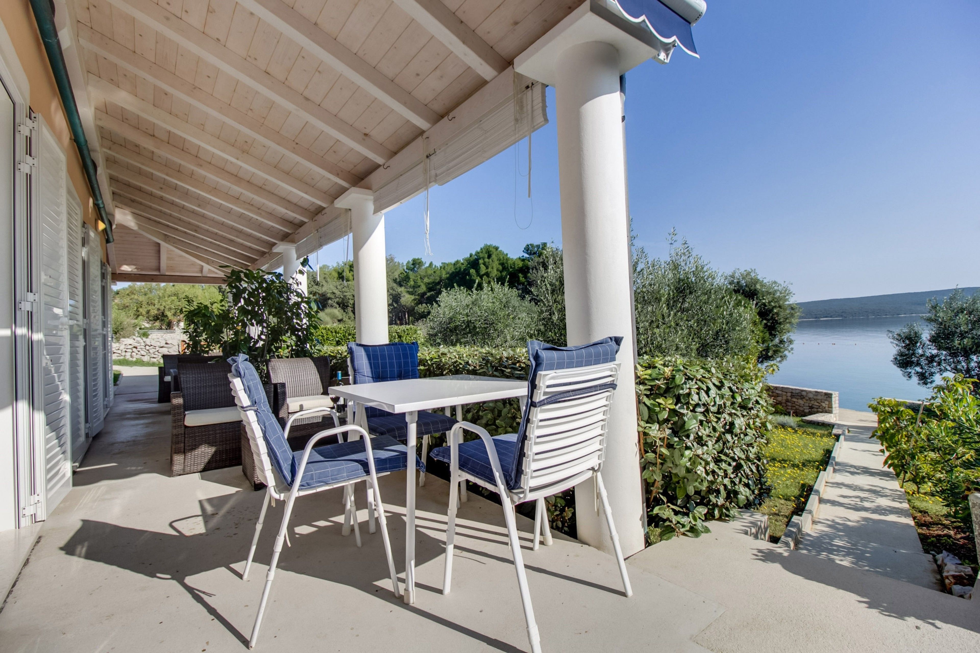 An outdoor patio with a table and chairs, a covered area with a wooden ceiling, and a view of the sea.