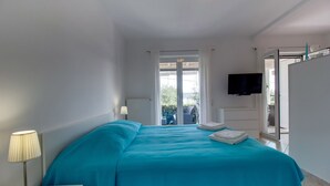 A bedroom with a bed, a TV mounted on the wall, and a view of the outdoors through a glass door. - Apartments Del Sole (Mali Losinj)