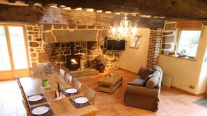 Ein gemütliches Wohnzimmer mit Kamin aus Stein, einer Essecke mit Holztisch und einer bequemen Couch.