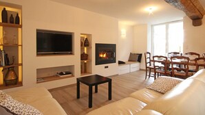 A modern living room with a fireplace, a television, and a dining area with wooden chairs and a table.