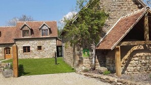A stone building with a tiled roof, a grassy area in front, and a sign indicating a Gîte.