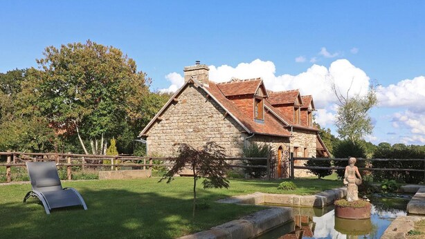 A stone house with a tiled roof, a small pond, and a statue in the garden.