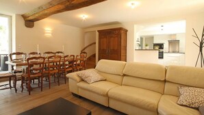 A living room with a sofa, wooden dining table, chairs, and a staircase.