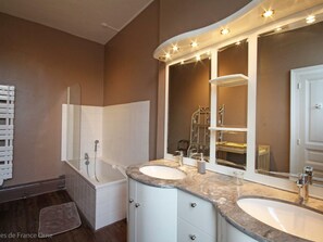 A modern bathroom with a bathtub, two sinks, and a large mirror with lights.