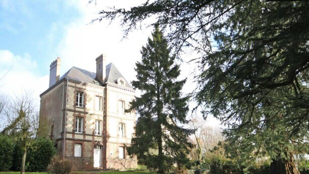 A large, historic building with multiple stories, surrounded by well-maintained lawns and mature trees.