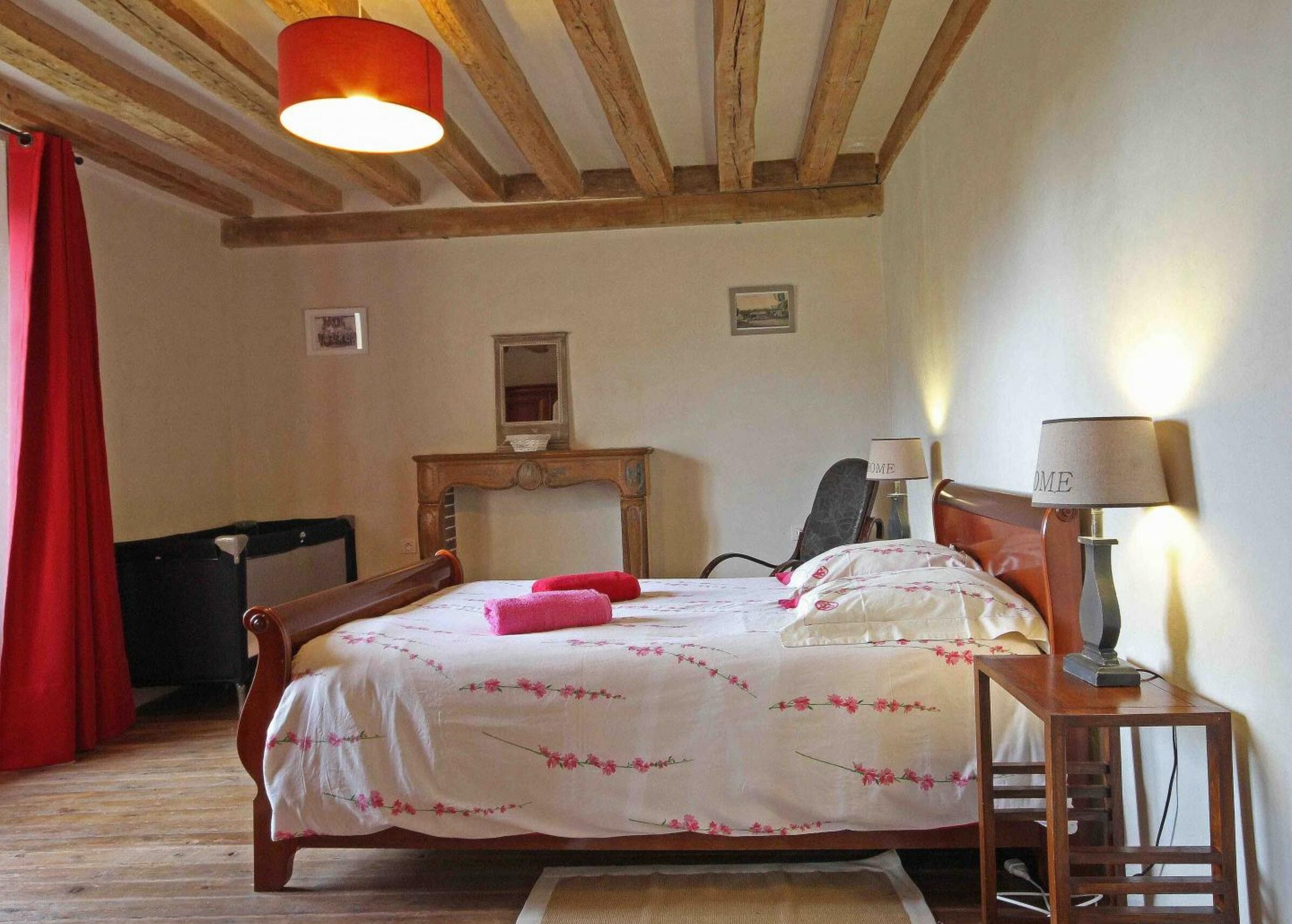 Ein Schlafzimmer mit einem hölzernen Bett, einem Nachttisch mit Lampe, einem Spiegel und einem Kamin.