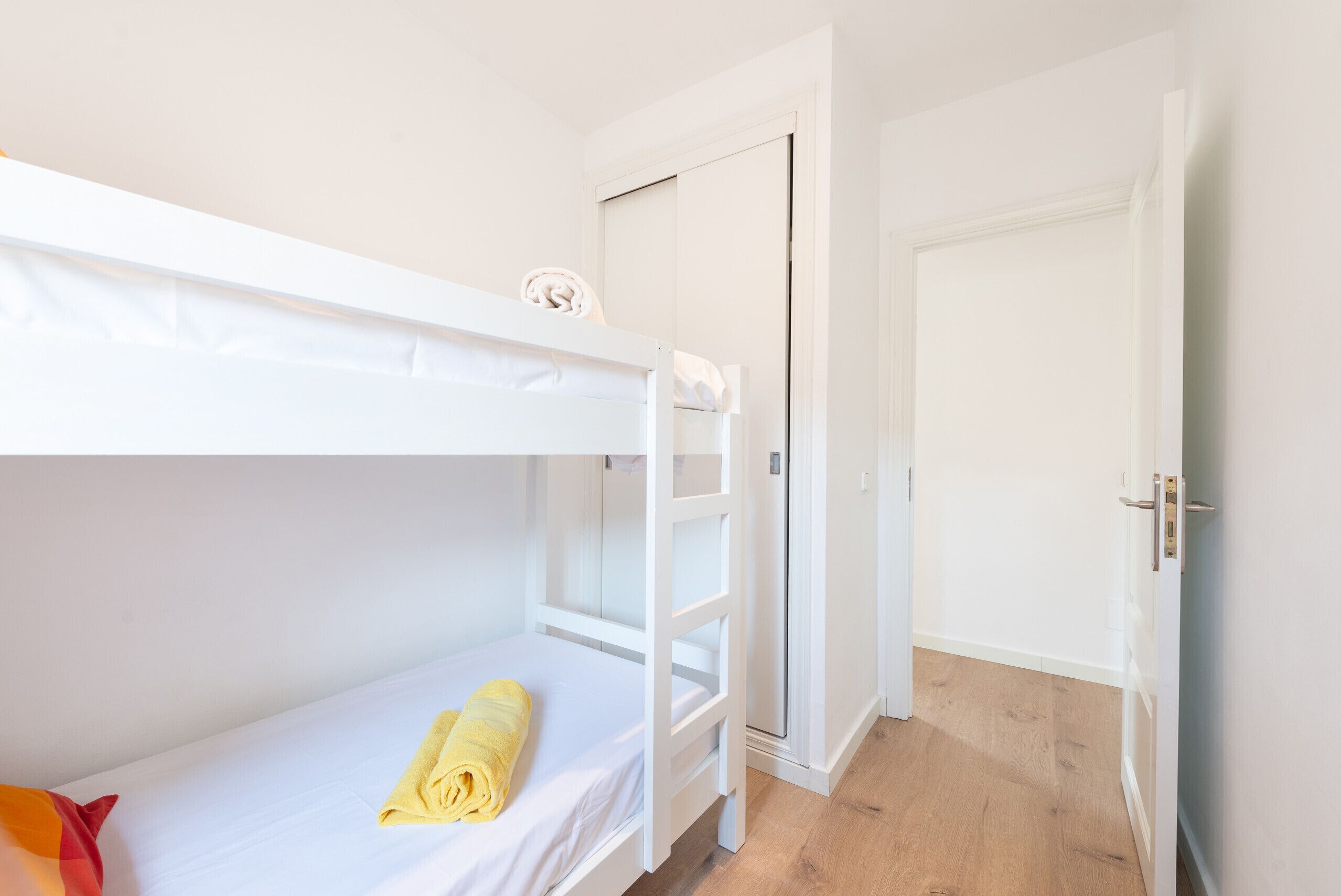 Quarto com beliche, porta branca e chão de madeira.