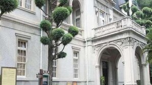 Un grand bâtiment historique doté d’une entrée imposante, de nombreuses fenêtres et d’un jardin bien entretenu avec des haies taillées.