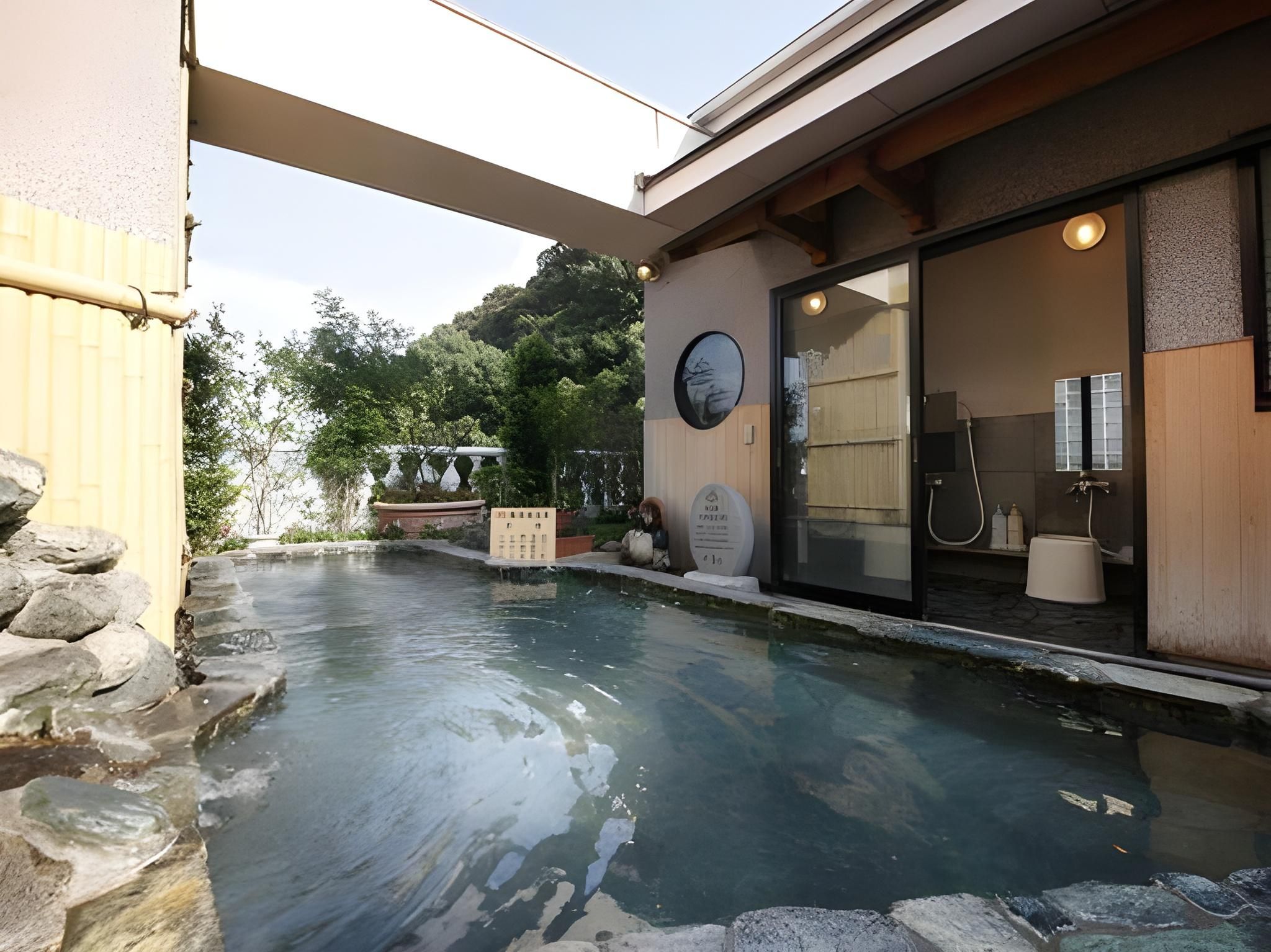 A spa pool with a stone border, a wooden deck, and a glass door leading to a bathroom.