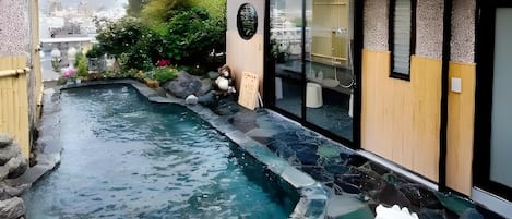 A hot spring area with a stone-lined pool, wooden deck, and a view of the cityscape.