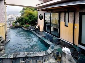 A hot spring area with a stone-lined pool, wooden deck, and a view of the cityscape.