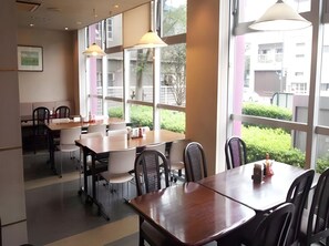 Un comedor con mesas y sillas, ventanas amplias e iluminación colgante.