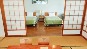 A traditional Japanese-style room with tatami flooring, two beds with green bedding, a nightstand, and a mirror reflecting the room.
