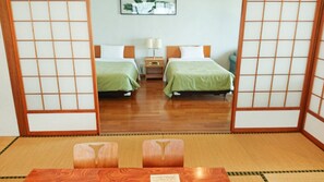 A traditional Japanese-style room with tatami flooring, two beds with green bedding, a nightstand, and a mirror reflecting the room.
