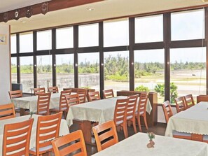 Un restaurant doté de nombreuses tables et chaises, de grandes fenêtres et offrant une vue sur l’extérieur.