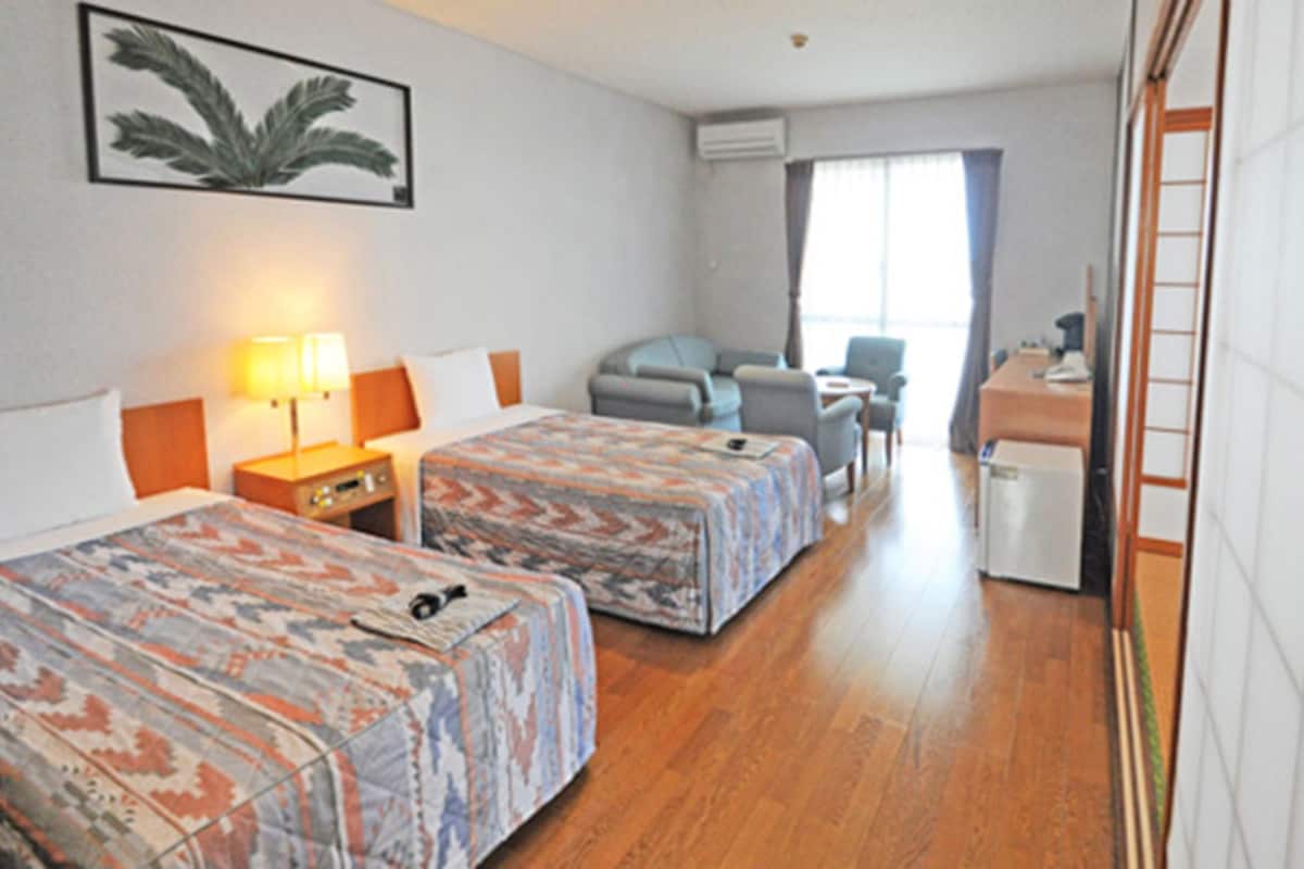 Une chambre d’hôtel avec deux lits, un bureau, une chaise et un petit réfrigérateur.