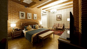 Un dormitorio con pared de ladrillo, vigas de madera en el techo, una cama con banco, una mesita de noche, una lámpara y un televisor.