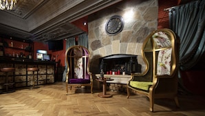 Una zona de bar con dos sillas ornamentadas, una chimenea de piedra y un reloj en la pared.