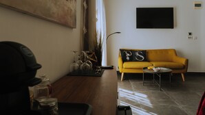 Un saló amb un sofà groc, una taula de centre i un televisor fixat a la paret.