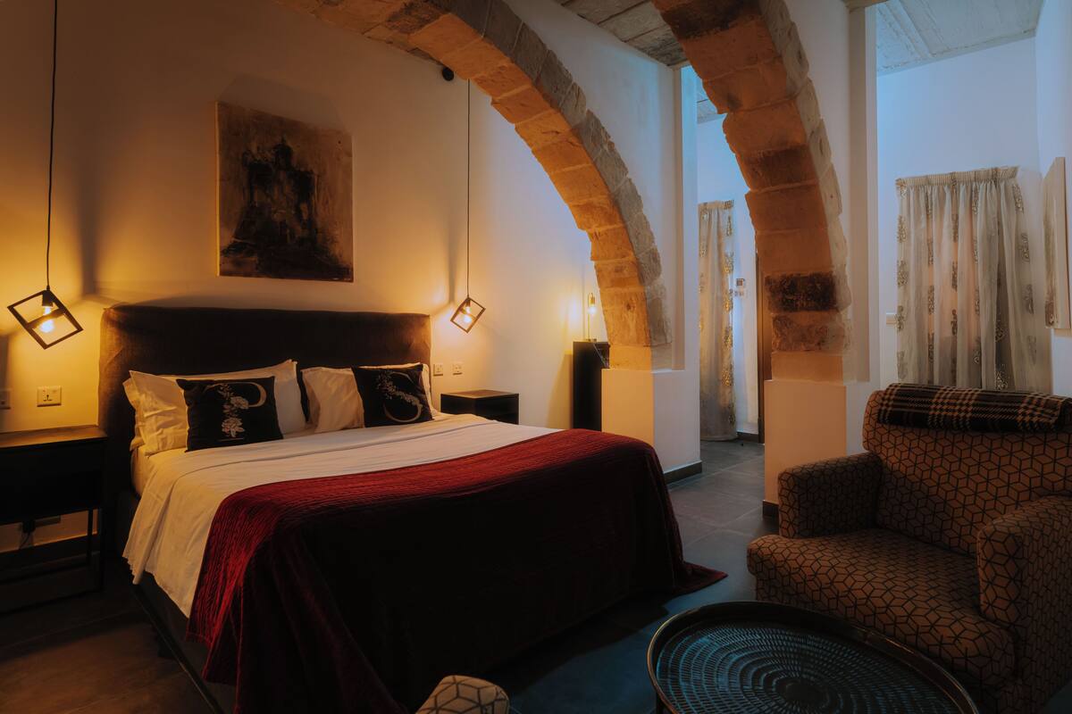Une pièce comprenant un lit, une chaise, une lampe et une structure en pierre en forme d’arc.