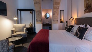 Una habitació d'hotel amb un llit, una cadira, un mirall rodó i un quadre a la paret.