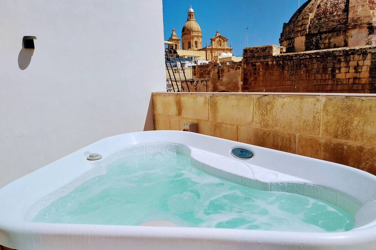 Un bain à remous doté d’un panneau de commande, installé devant un bâtiment historique et un mur de pierre.