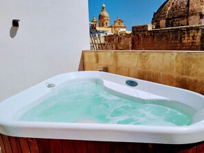 Un bain à remous doté d’un panneau de commande, installé devant un bâtiment historique et un mur de pierre.