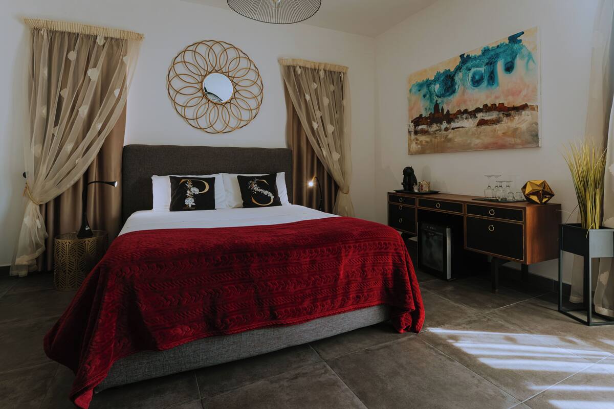 Une chambre à coucher avec un lit, des rideaux, un tableau, une commode et un vase.