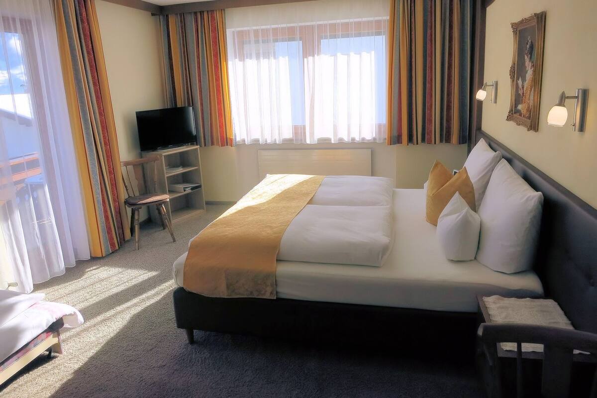 Quarto de hotel com uma cama grande, televisão, escrivaninha e uma cadeira.