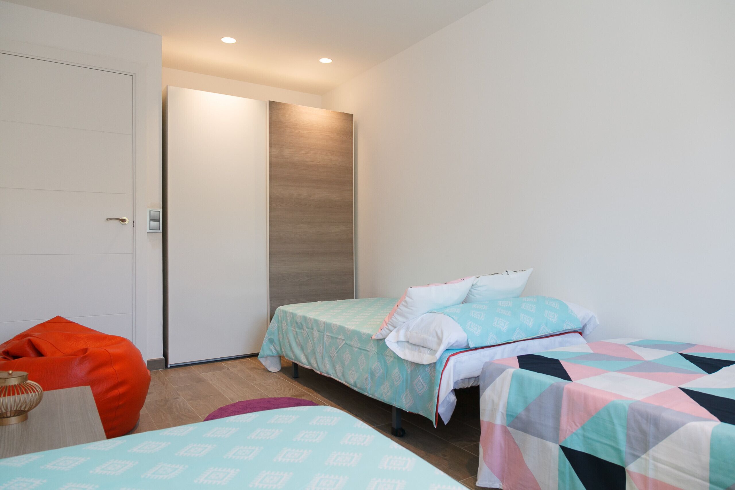 A modern bedroom with two beds, a red bean bag chair, and a wooden panel wall.