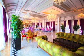 A spacious lobby with a green sofa, a large potted plant, and a chandelier.