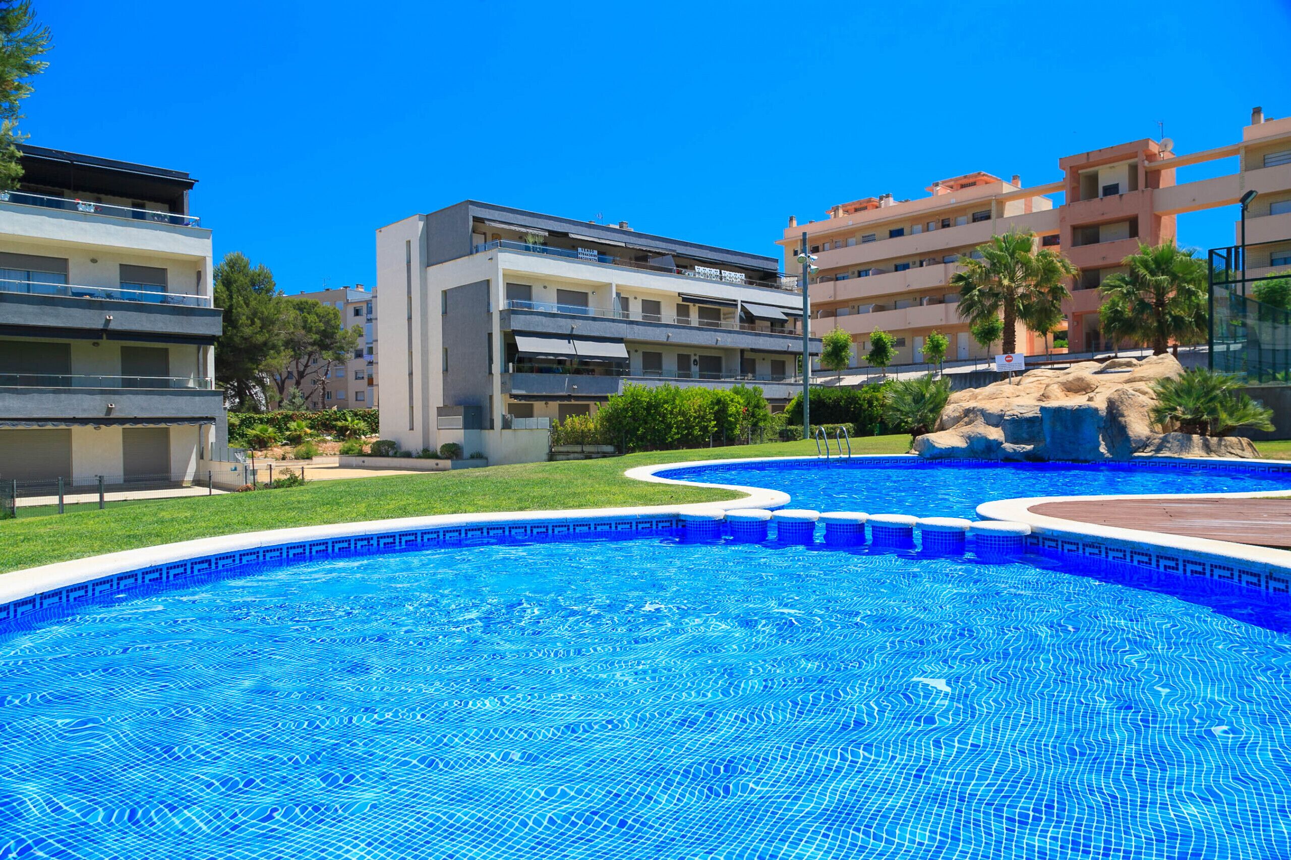 Una piscina rodeada de edificios modernos con balcones y un cielo azul despejado.