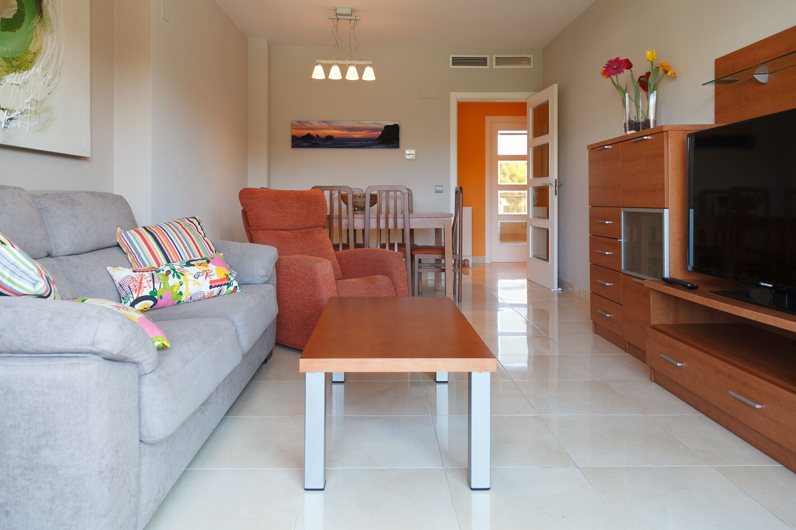 A modern living room with a grey sofa, a wooden coffee table, and a TV stand.