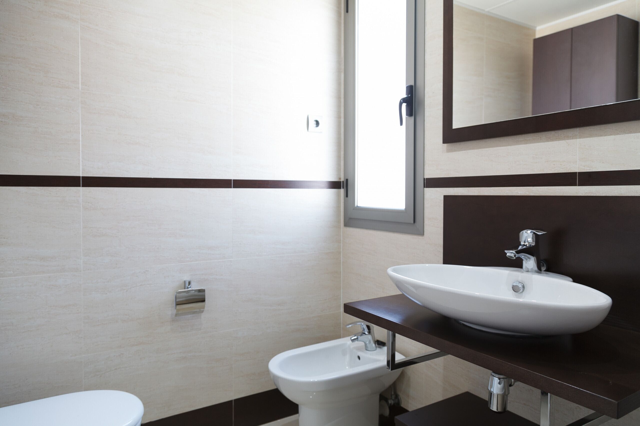 Een moderne badkamer met een wit wastafelmeubel, een bidet en een spiegel boven het wastafelmeubel.