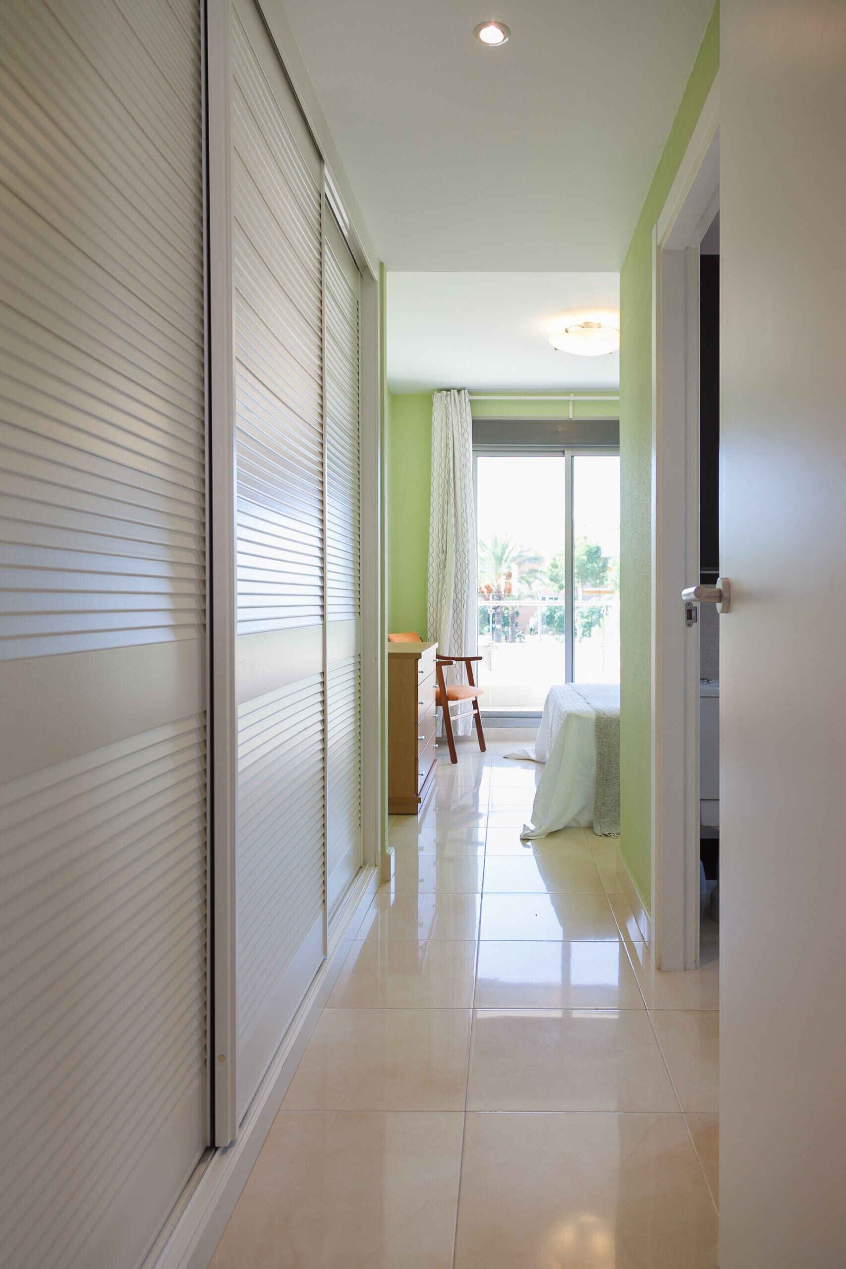 A hallway with a sliding door, a chair, and a bed in the background.