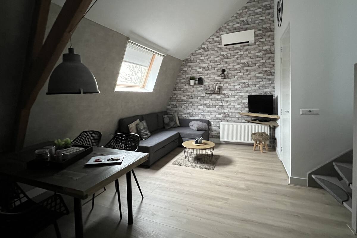A loft-style living space with a sloped ceiling, exposed brick wall, and a built-in TV shelf.