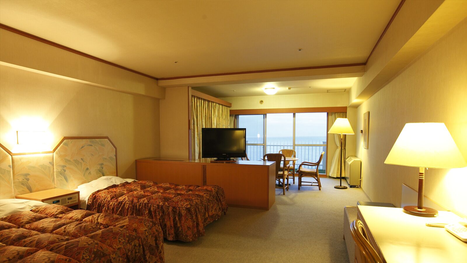 A hotel room with a bed, a desk, a television, a chair, and a view of the ocean.