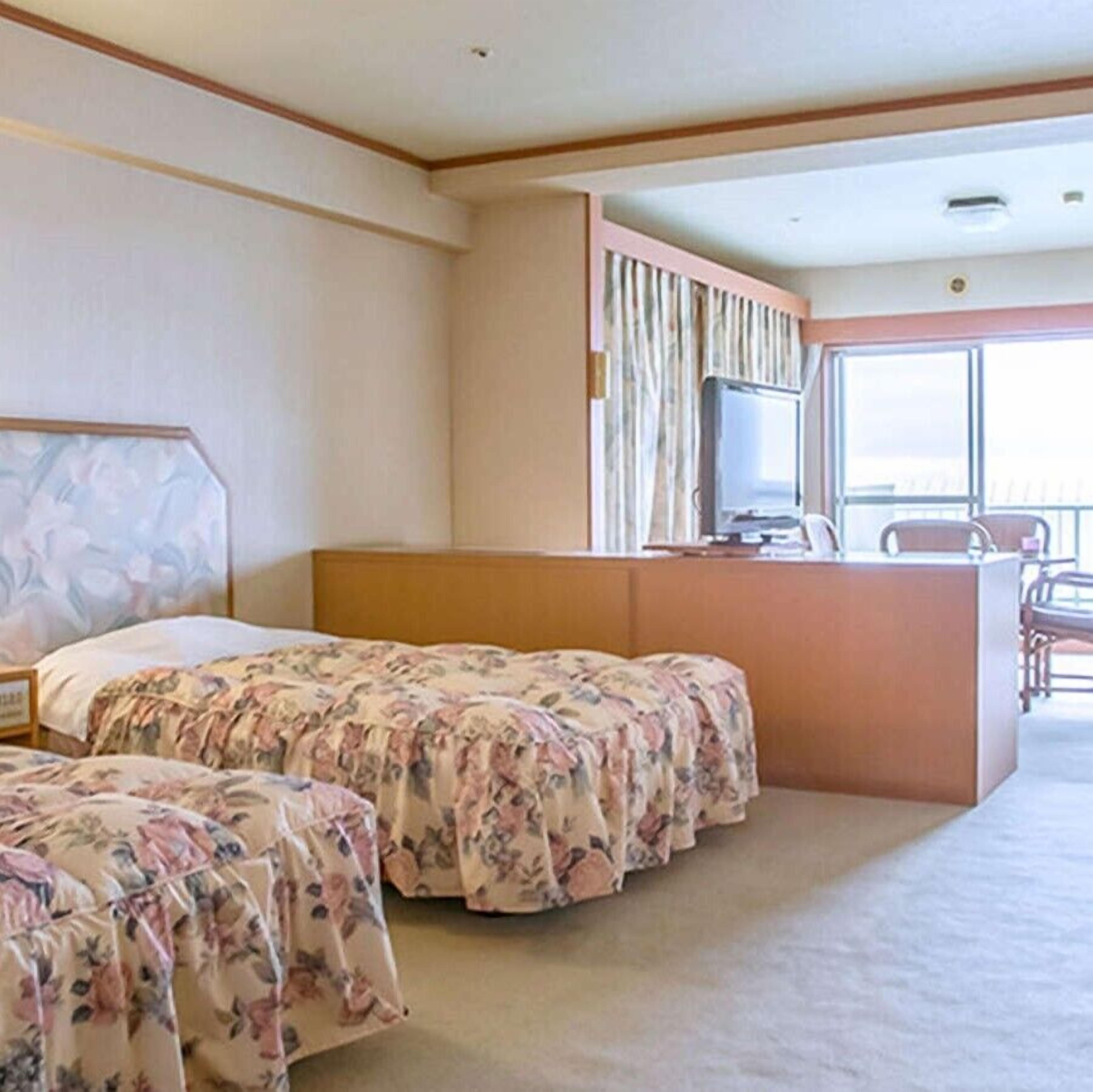 Una habitación de hotel con dos camas, televisión, escritorio y ventana.