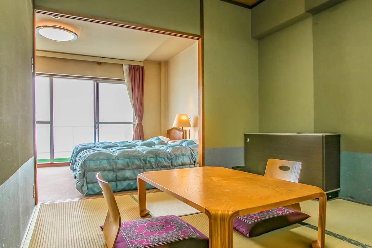 A room with a bed, a table, a chair, a lamp, and a refrigerator.