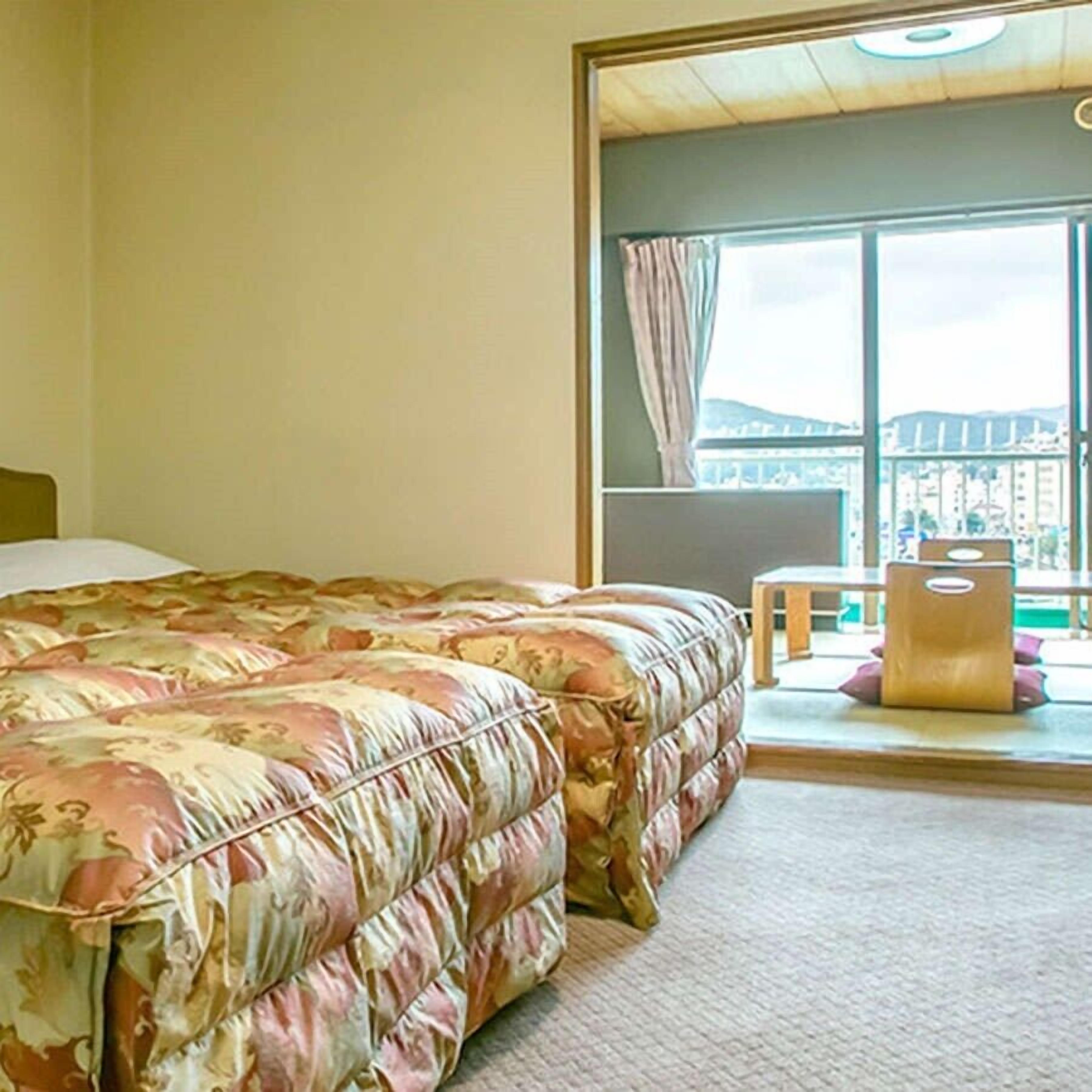 A bedroom with a large bed, a window with a view, and a small table with a bag.